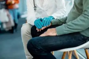 Unrecognizable doctor wearing protective glove while comforting senior patient in a hallway at medical clinic.